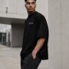 Side profile of a male model wearing a black Birmingham Signature oversized heavyweight T-shirt with relaxed fit and subtle white chest coordinates design.