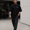 Male model walking through contemporary Birmingham-inspired architecture wearing a black Birmingham Signature oversized heavyweight T-shirt with minimalist white chest print.