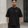 Male model wearing a black Birmingham Signature oversized heavyweight T-shirt with white chest coordinates print against contemporary Birmingham-inspired architecture.