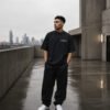 Male model wearing a black London Signature coordinates oversized T-shirt on a modern concrete rooftop with city skyline, minimalist premium streetwear editorial.