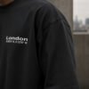 Close-up of shoulder and sleeve on black oversized heavyweight T-shirt showing premium cotton texture, drop shoulder construction and minimalist London chest print.