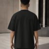 Rear view of a male model wearing a black Manchester Signature oversized heavyweight T-shirt with dropped shoulders and clean minimalist design.