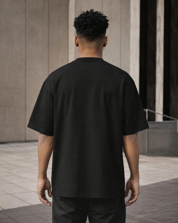 Rear view of a male model wearing a black Manchester Signature oversized heavyweight T-shirt with dropped shoulders and clean minimalist design.