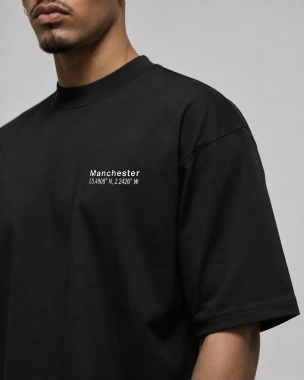 Close-up of the Manchester Signature chest print on a black oversized heavyweight T-shirt showing premium cotton fabric and clean white design.