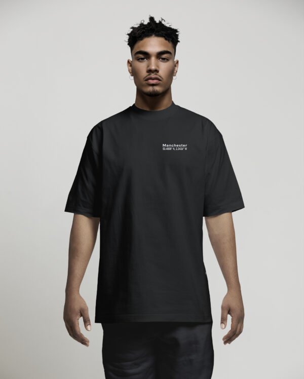 Front view of a male model wearing a black Manchester Signature oversized heavyweight T-shirt featuring a minimalist white left chest coordinates print.