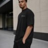 Side profile of a male model wearing a black Manchester Signature oversized heavyweight T-shirt with relaxed fit and subtle white chest coordinates design.