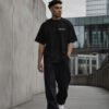 Male model walking through contemporary Manchester-inspired architecture wearing a black Manchester Signature oversized heavyweight T-shirt with minimalist white chest print.