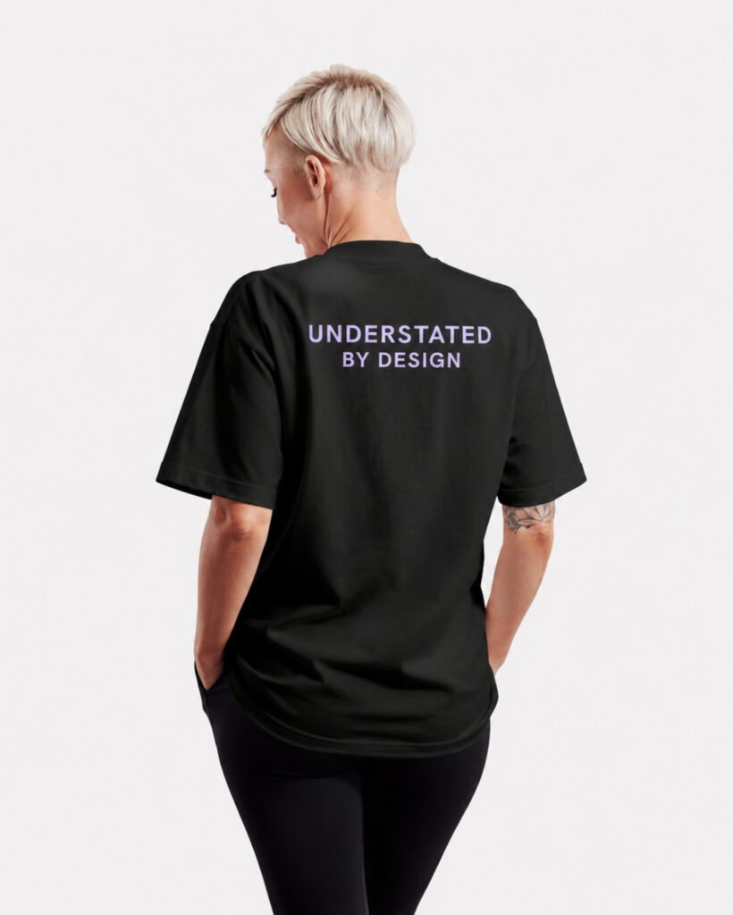 Lilac Capsule 2 Rear view of a black Kat Krush oversized T-shirt featuring the Understated By Design statement print across the upper back in a minimalist studio setting.