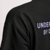 Close-up of the heavyweight cotton fabric and shoulder seam on a black Kat Krush oversized T-shirt, highlighting the Understated By Design back print.