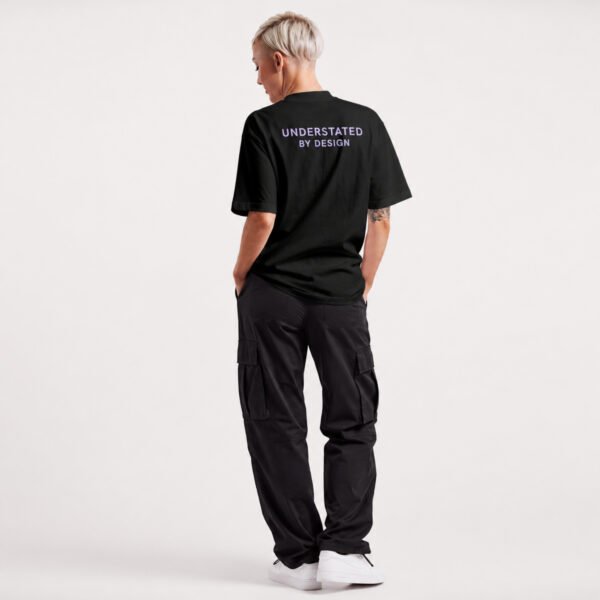 Kat Krush oversized black heavyweight T-shirt with Understated By Design back print, shown on a model wearing black cargo trousers in a relaxed rear pose.