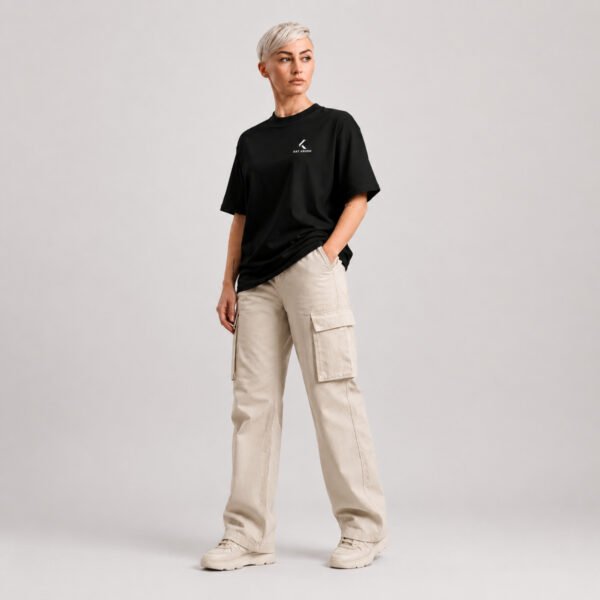 Full-length front view of a female model wearing a black oversized Kat Krush heavyweight T-shirt with a minimalist white chest logo and relaxed off-white cargo trousers.