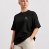 Female model wearing a black oversized Kat Krush heavyweight T-shirt with a minimalist white chest logo, styled with off-white cargo trousers in a clean studio setting.