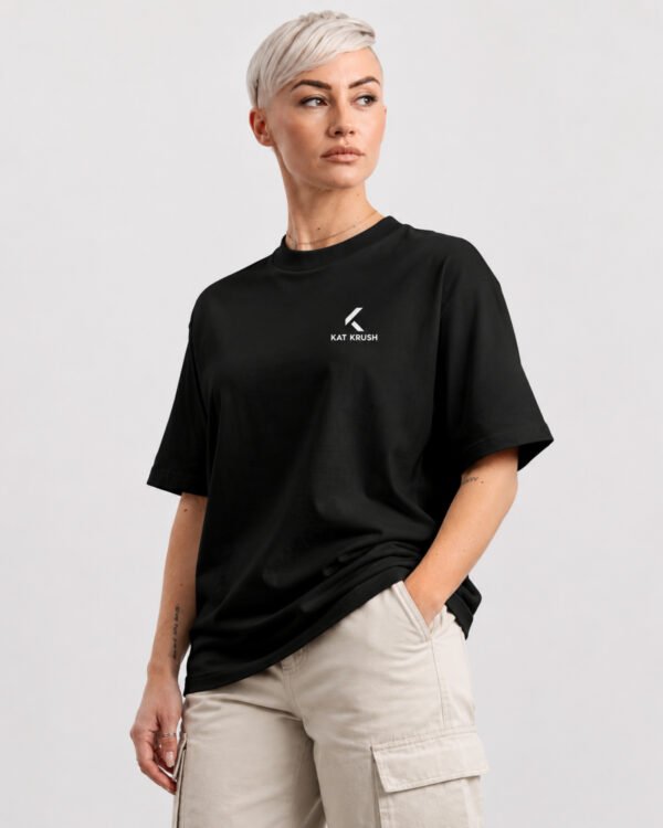 Female model wearing a black oversized Kat Krush heavyweight T-shirt with a minimalist white chest logo, styled with off-white cargo trousers in a clean studio setting.