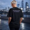 Model wearing a black Kat Krush oversized T-shirt with Understated By Design back print overlooking the London skyline at dusk, embodying minimalist streetwear and quiet confidence.