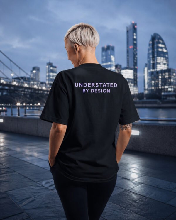Model wearing a black Kat Krush oversized T-shirt with Understated By Design back print overlooking the London skyline at dusk, embodying minimalist streetwear and quiet confidence.