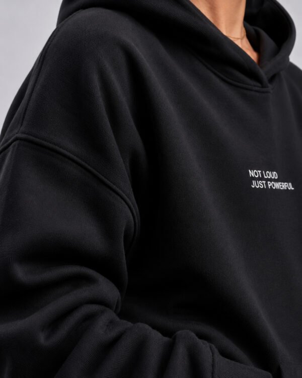 Close-up of the black Kat Krush oversized hoodie showcasing heavyweight premium fabric, dropped shoulder construction and minimalist "Not Loud Just Powerful" chest print.