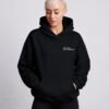 Front studio view of a woman wearing a black oversized Kat Krush hoodie featuring the minimalist "Not Loud Just Powerful" chest print and relaxed heavyweight fit.