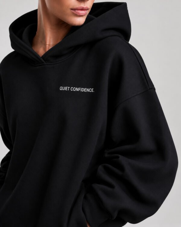 Close-up of the Kat Krush oversized black heavyweight hoodie showcasing the "Quiet Confidence." chest print, premium heavyweight fabric and dropped shoulder construction.