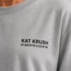 "Close-up of Heather Grey oversized t-shirt featuring black Kat Krush London coordinates chest logo. Premium heavyweight cotton fabric with minimalist streetwear design."