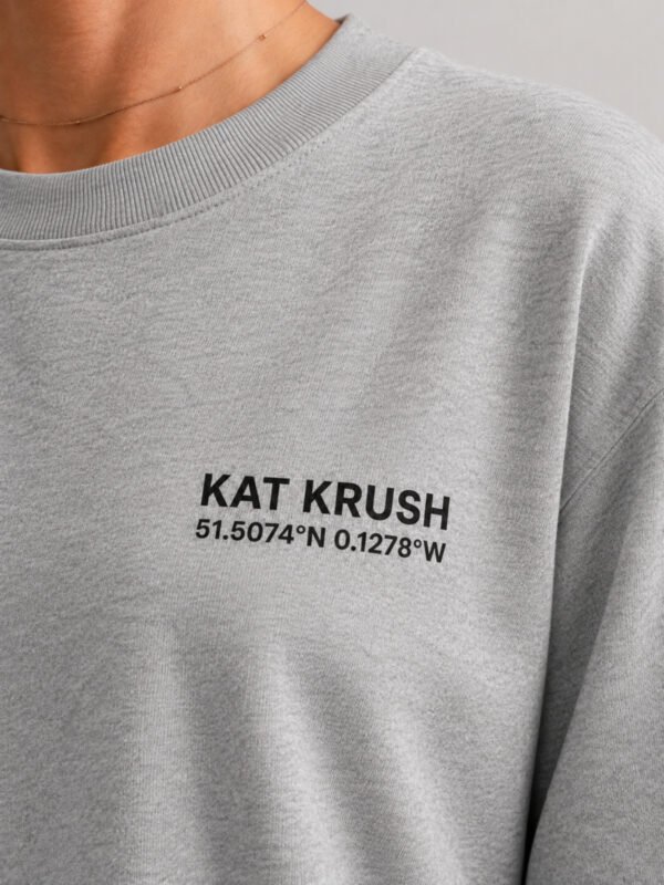 "Close-up of Heather Grey oversized t-shirt featuring black Kat Krush London coordinates chest logo. Premium heavyweight cotton fabric with minimalist streetwear design."