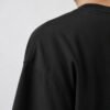 Close-up of the shoulder and neckline of a black oversized Kat Krush heavyweight cotton T-shirt, highlighting the smooth fabric texture, dropped shoulder seam and premium construction.