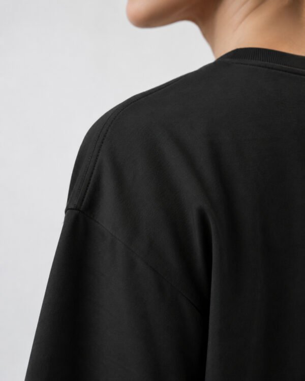 Close-up of the shoulder and neckline of a black oversized Kat Krush heavyweight cotton T-shirt, highlighting the smooth fabric texture, dropped shoulder seam and premium construction.