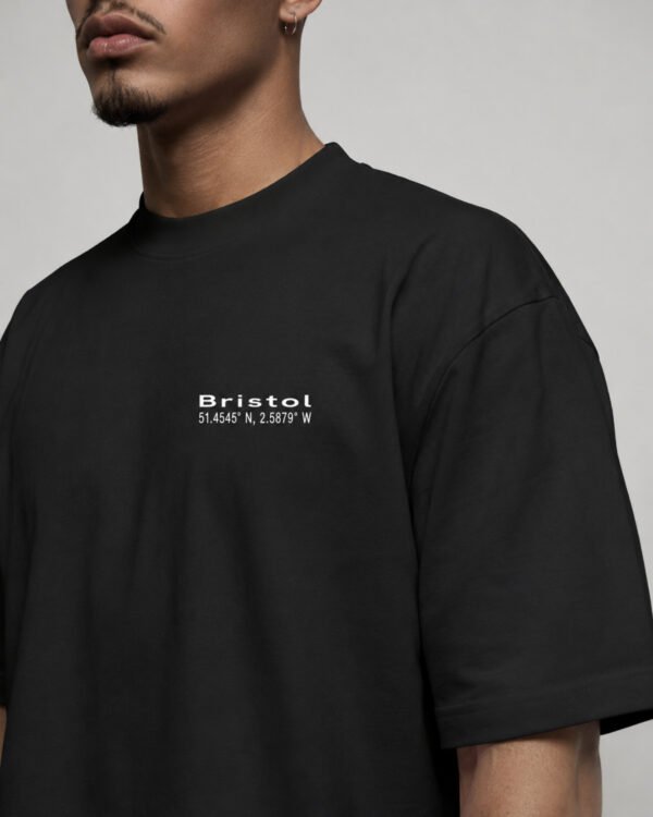 Close-up of the Bristol Signature chest print on a black oversized heavyweight T-shirt showing premium heavyweight cotton fabric and clean white coordinates design.