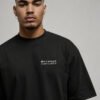 Portrait close-up of a male model wearing a black Bristol Signature oversized heavyweight T-shirt with subtle white left chest coordinates print.