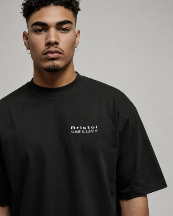 Portrait close-up of a male model wearing a black Bristol Signature oversized heavyweight T-shirt with subtle white left chest coordinates print.
