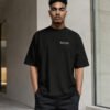 Front view of a male model wearing a black Bristol Signature oversized heavyweight T-shirt with minimalist white left chest coordinates print in a modern architectural setting.