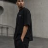 Side profile of a male model wearing a black Bristol Signature oversized heavyweight T-shirt with relaxed fit and subtle white chest coordinates design.