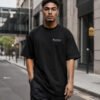 Male model walking through contemporary Bristol-inspired architecture wearing a black Bristol Signature oversized heavyweight T-shirt with minimalist white chest print.