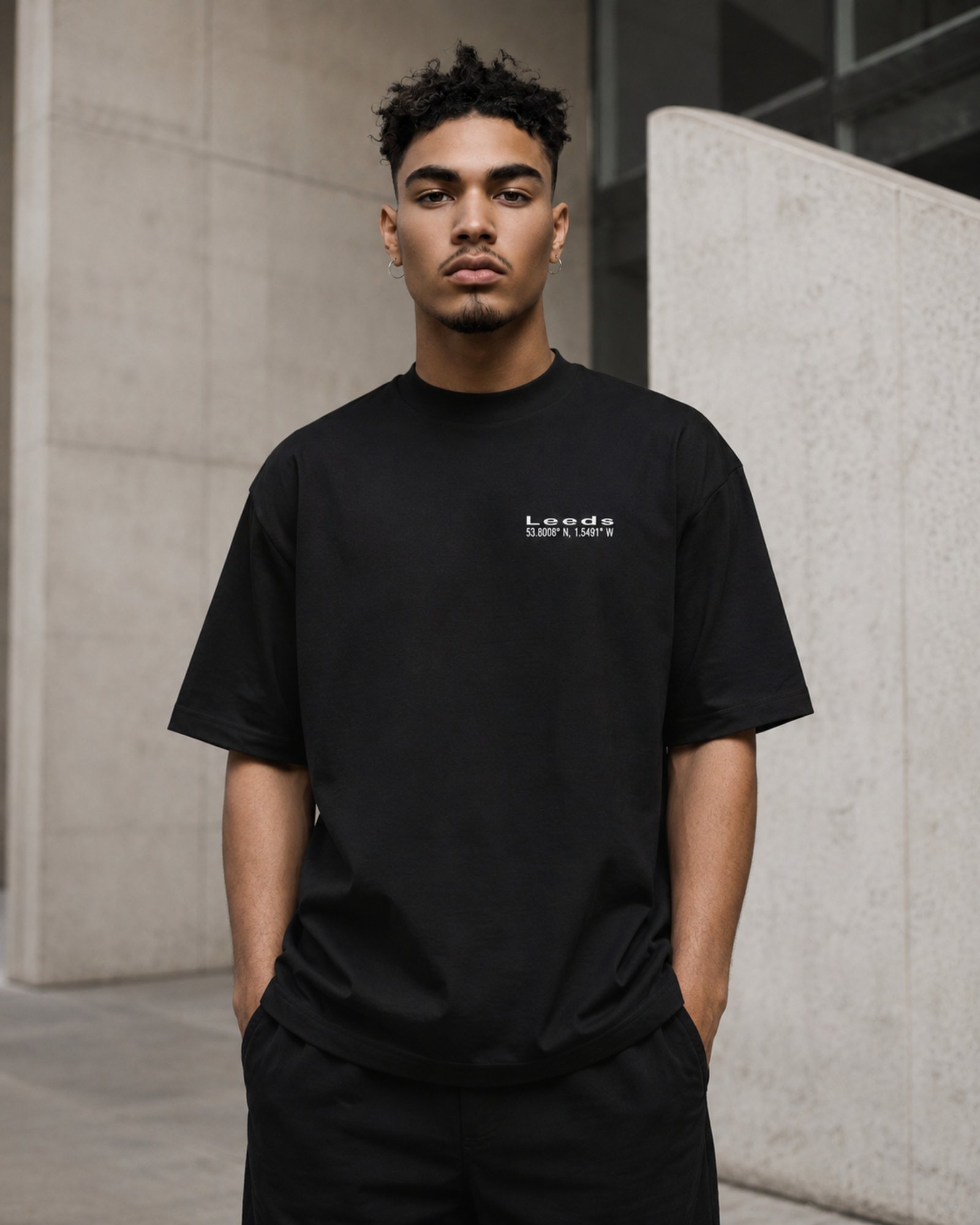 Male model wearing a black Leeds Signature oversized T-shirt against contemporary Leeds architecture.