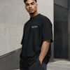 Male model in a relaxed three-quarter pose wearing a black Leeds Signature oversized T-shirt with white Leeds coordinates chest design.