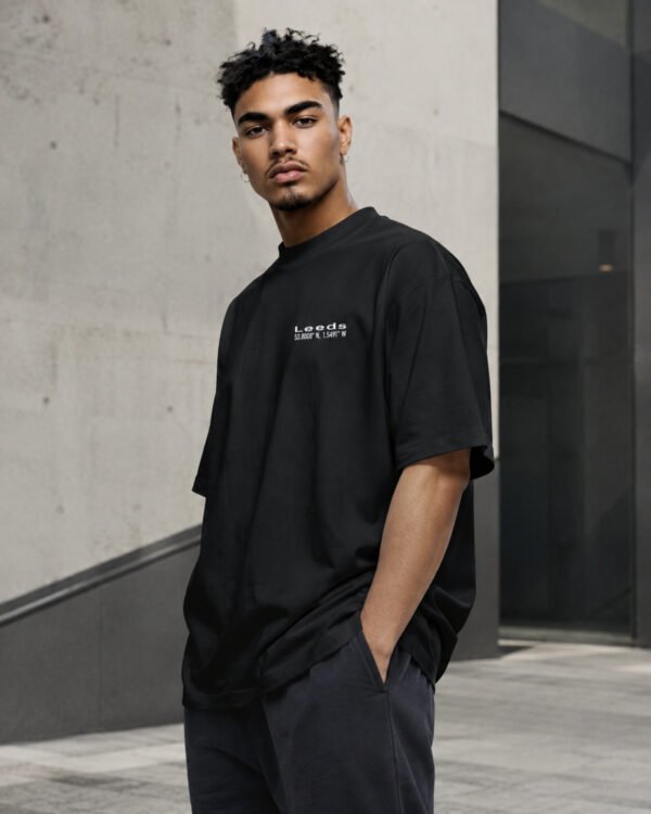 Male model in a relaxed three-quarter pose wearing a black Leeds Signature oversized T-shirt with white Leeds coordinates chest design.