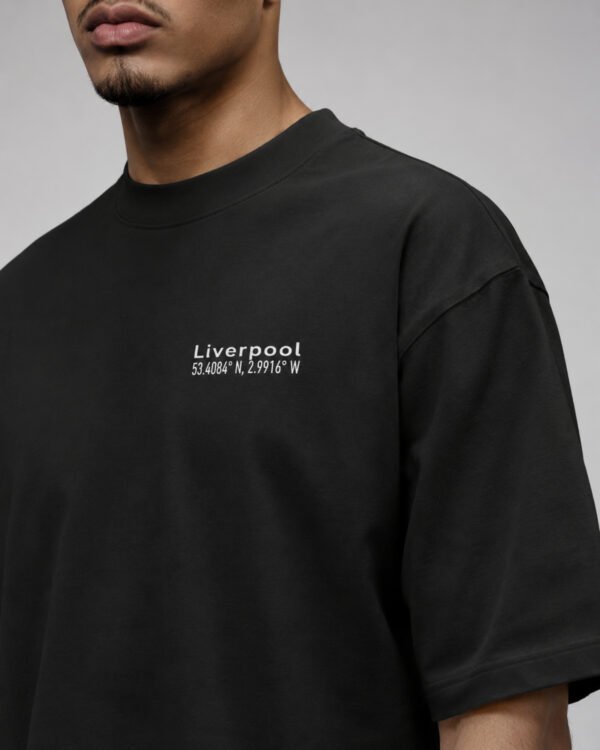 Close-up of the Liverpool Signature chest print on a black oversized heavyweight T-shirt showing the white city coordinates design and heavyweight fabric.