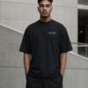 Male model wearing a black Liverpool Signature oversized heavyweight T-shirt with subtle white chest coordinates print against contemporary architecture.