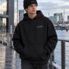 Male model wearing black Kat Krush fisherman beanie and black Liverpool Signature heavyweight hoodie in a contemporary waterfront setting