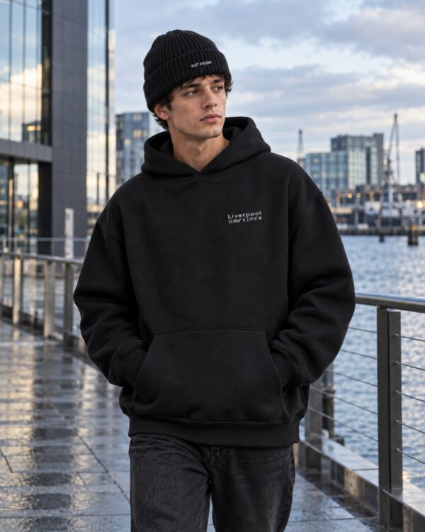 Male model wearing black Kat Krush fisherman beanie and black Liverpool Signature heavyweight hoodie in a contemporary waterfront setting