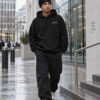 Male model walking in black Kat Krush fisherman beanie and London Signature heavyweight hoodie through contemporary London architecture