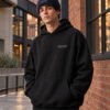 Male model wearing French Navy Kat Krush fisherman beanie and black Manchester Signature heavyweight hoodie in red brick Manchester architecture
