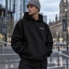 Male model wearing grey Kat Krush fisherman beanie and black Leeds Signature heavyweight hoodie in contemporary Leeds architecture