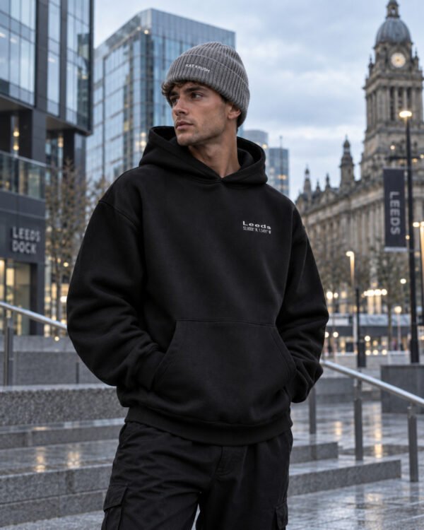 Male model wearing grey Kat Krush fisherman beanie and black Leeds Signature heavyweight hoodie in contemporary Leeds architecture