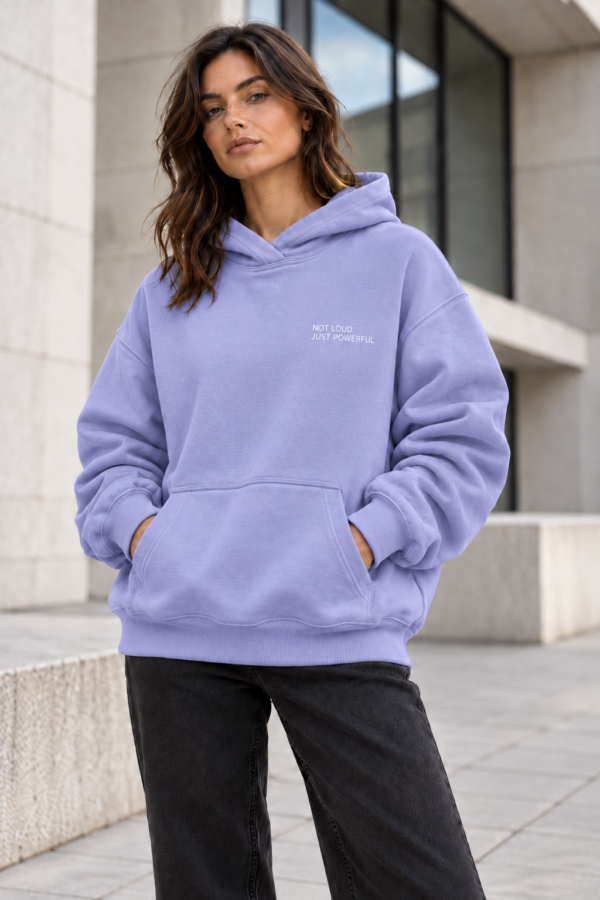kk Lavender Hoodie Urban Portrait Female model wearing Kat Krush Not Loud Just Powerful violet oversized hoodie with dark jeans in a contemporary British architectural setting.