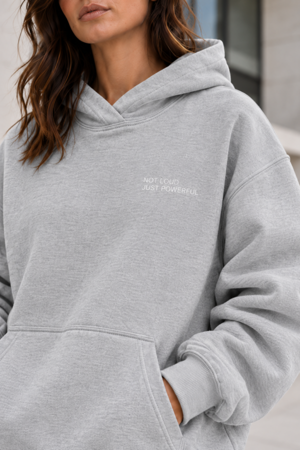 kk Not Loud, Just Powerful Hoodie Close-up of Kat Krush Not Loud Just Powerful oversized hoodie in heather grey, showing heavyweight fabric texture, white chest print and ribbed cuff.